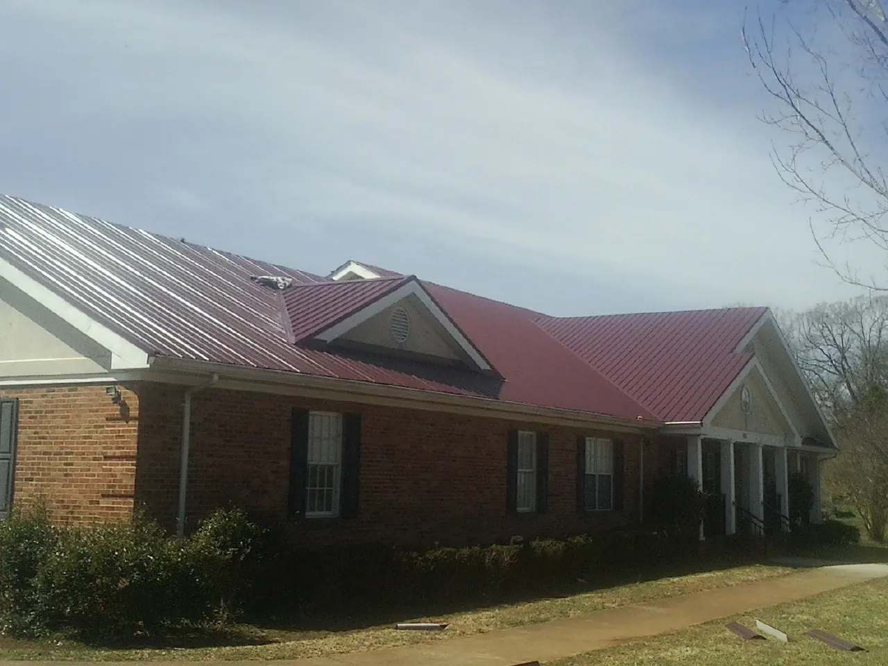 Red metal roof with gabled entries on a long brick building, from a Hail Damage Roof Repair job in Verdon