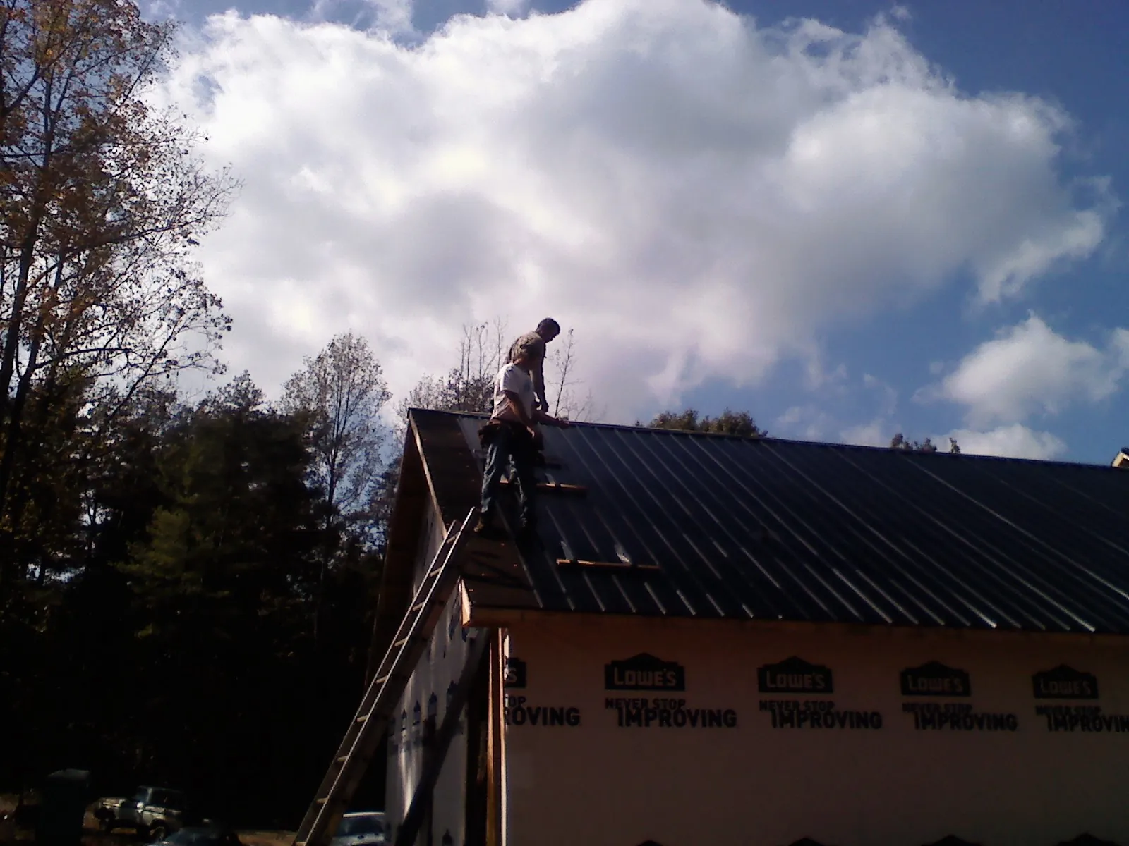 Roofer fastening dark metal panels high against a cloudy sky, from a Roof Inspection job in Verdon