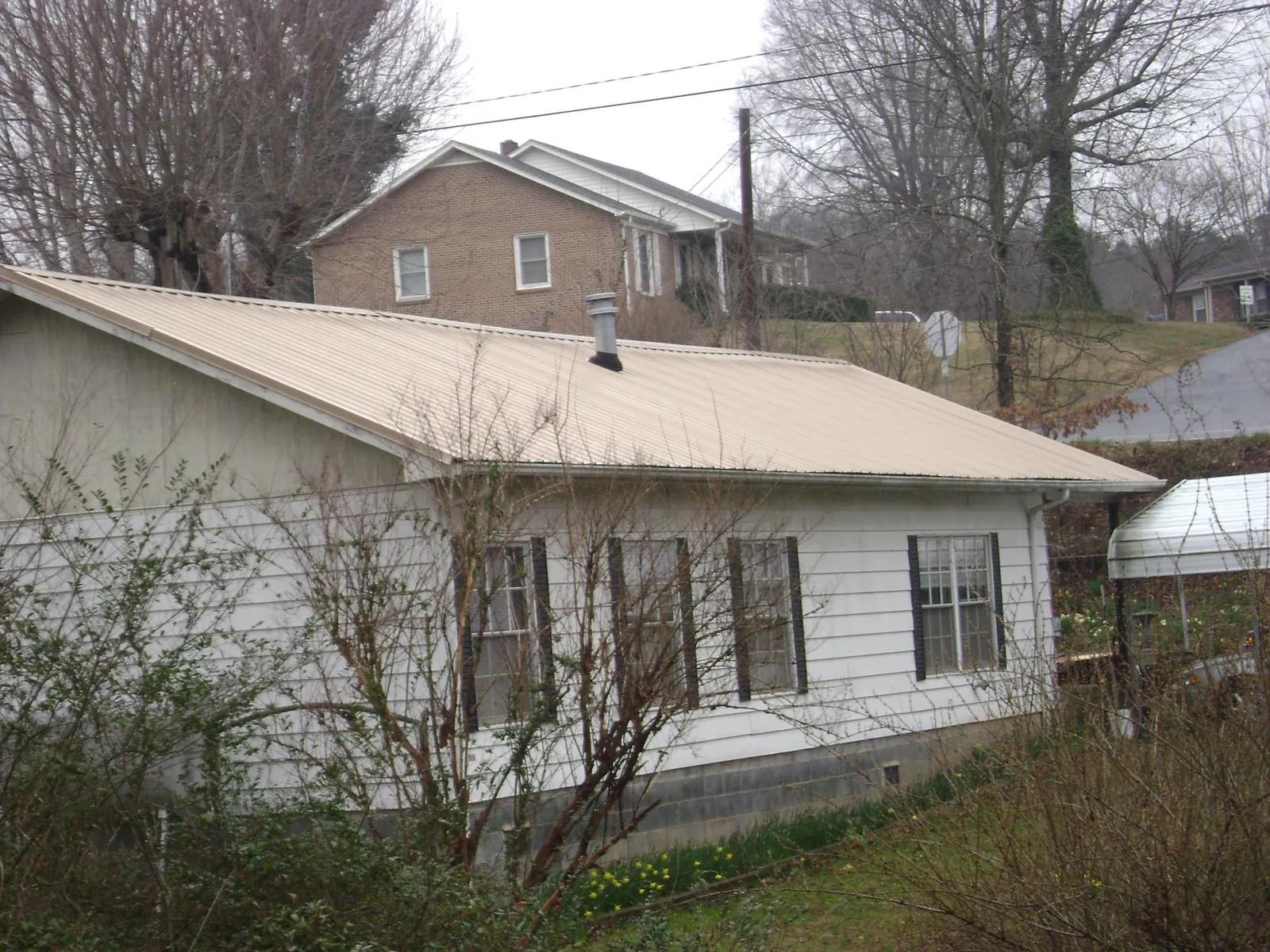 Tan metal roof on a white sided house set into a hillside — Commercial Roofing by Roofing Brothers in Verdon